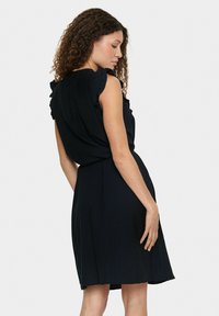Abito nero con dettagli arricciati sulle spalle, una vestibilità comoda e gonna a campana. Texture liscia e design fino al ginocchio.
