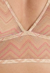 Bralette in pizzo beige con un motivo a zigzag rosa. Presenta una scollatura a V, bordi smerlati e dettagli fini lungo le cuciture.