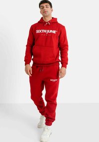 Conjunto de sudadera roja y joggers fabricado en tejido suave, con un bolsillo delantero, capucha con cordón y acentos de logo en blanco.