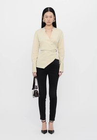 Beige wrap krekls ar garām piedurknēm, sasiets ap jostasvietu, apvienots ar melniem pieguļošiem džinsiem un norādītas pirkstveidīgām kurpēm. Mazs pleca somiņa rokā.