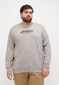 Sweatshirt en coton gris à manches longues, avec des bords côtelés aux poignets et à la taille. Présente un logo noir imprimé sur la poitrine. Convient pour une tenue décontractée.