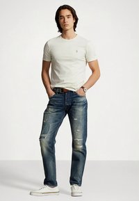 Balti medvilninė marškinėliai su mažu logotipu, derinami su suplėšytais mėlynais džinsais su pleistrais. Aprangą užbaigia balti sportbačiai.