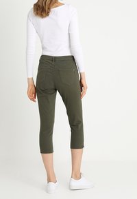Pantalones recortados verde oliva con una tela suave y un detalle de cremallera en el dobladillo, combinados con una blusa blanca de manga larga ajustada.