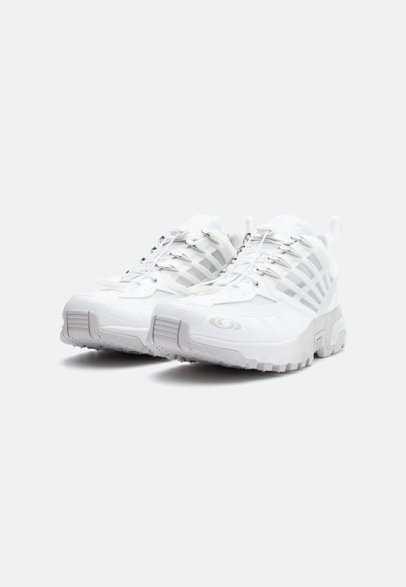 Weiße Sportschuhe verfügen über ein strukturiertes Obermaterial mit Mesh-Einsätzen, eine dicke, gepolsterte Sohle und ein einzigartiges Schnürsystem für einen sicheren Sitz.