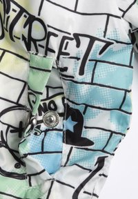 Tela colorida con un diseño estilo graffiti en tonos azul, verde y negro; incluye un detalle de botón a presión plateado.