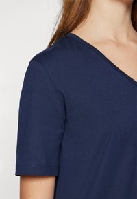 Námořnická modrá v-neck tričko vyrobené z hladké látky, s krátkými rukávy a čistým výstřihem. Žádné viditelné vzory ani akcenty.