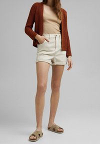 Rust-colored cardigan, beige ribbed top, cream shorts with rolled hem, and tan cross-strap sandals. Textured knit and casual style.