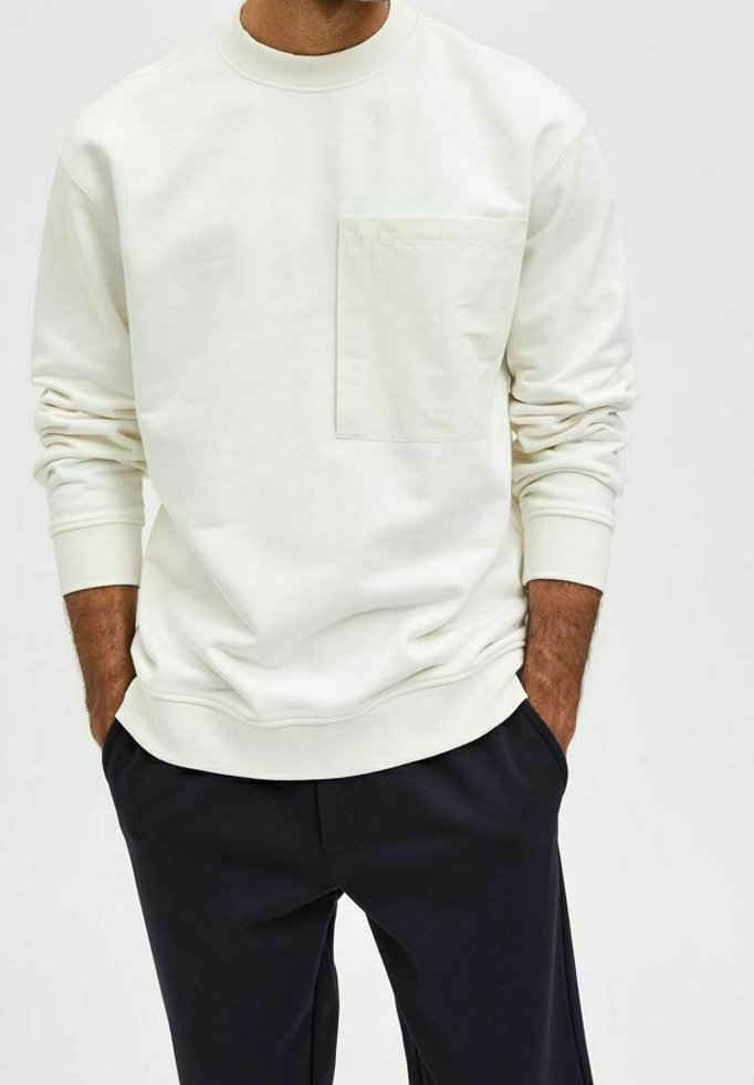 Vit crewneck sweatshirt i mjukt tyg, med en frontficka och ribbad mudd, i kombination med mörka byxor.