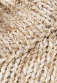 Tissu tricoté beige mettant en valeur des variations de fil épais et fin, avec une surface texturée, douce et des motifs étroitement tissés.