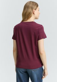 T-shirt bordeaux à manches courtes avec un col rond et une coupe décontractée, associé à un jean bleu, mettant en valeur une texture en coton lisse.
