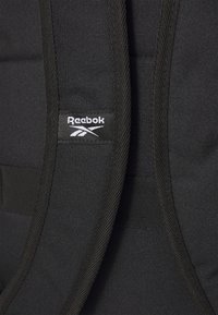 Zwarte Reebok rugzak van een gestructureerde stof, met een opvallende logopatch en verstelbare schouderbanden, die duurzame materialen en stiksels toont.