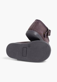 Zapato de tela púrpura con suela de goma negra, que presenta una hebilla lateral y una parte superior texturizada, diseñado para la comodidad y el estilo.