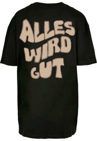 Čierne oversize tričko s nápisom "ALLES WIRD GUT" v béžovej farbe, s tučným, vlnitým písmom na chrbte.