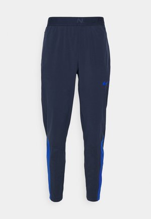 Męskie granatowe sportowe spodnie z zwężanymi nogawkami, elastycznym pasem i niebieskimi bocznymi akcentami, z małym niebieskim logo Nike w kształcie łyżwy.