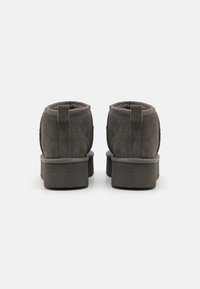 Paire de bottines en daim gris foncé à talons carrés vues de dos sur un fond blanc uni.