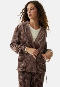 Blazer de terciopelo en un tono mauve suave con una textura blanda, dos bolsillos frontales, cuello de muesca y cintura ajustable con cordón.