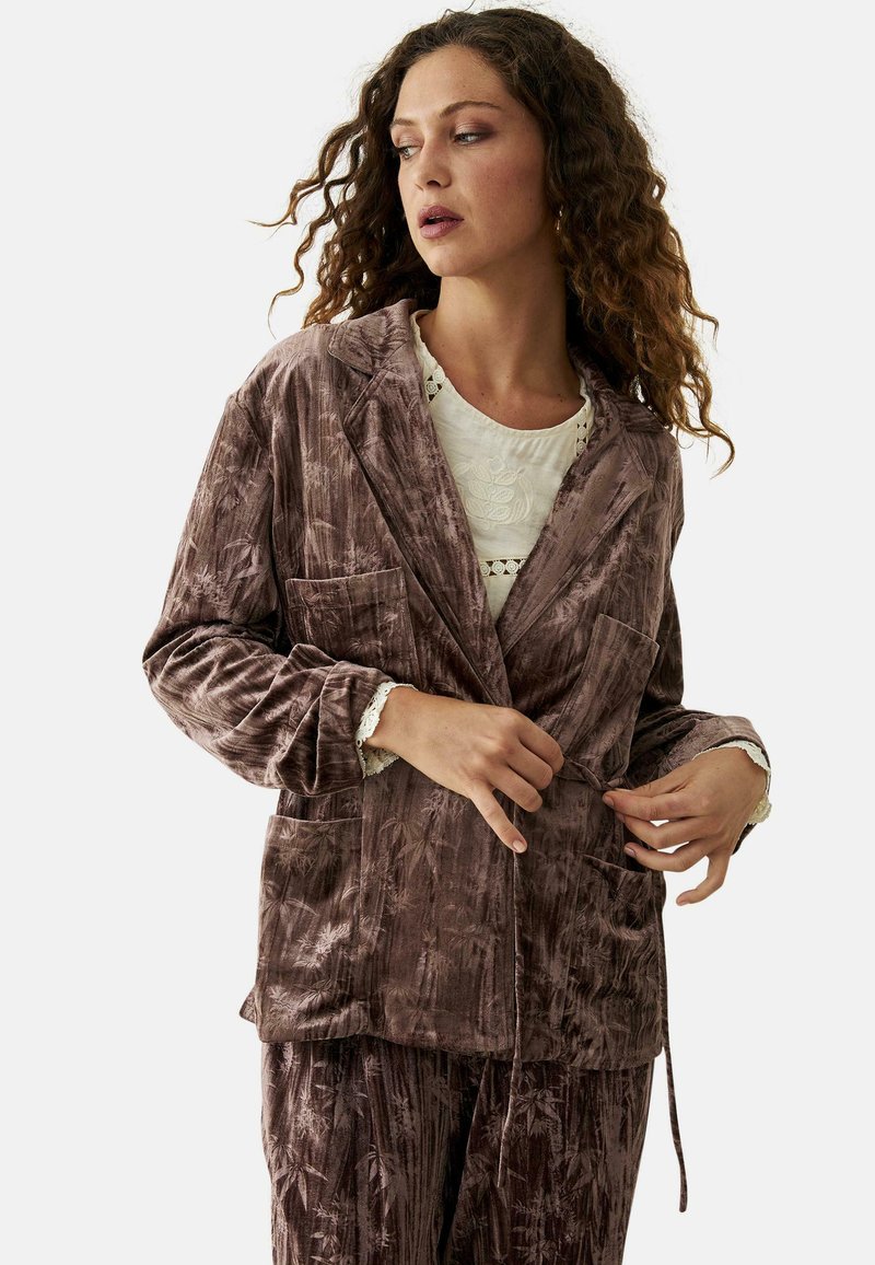 Blazer de terciopelo en un tono mauve suave con una textura blanda, dos bolsillos frontales, cuello de muesca y cintura ajustable con cordón.