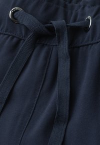 Ceinture en tissu bleu marine avec un cordon plat noué passant à travers des œillets en métal argenté.