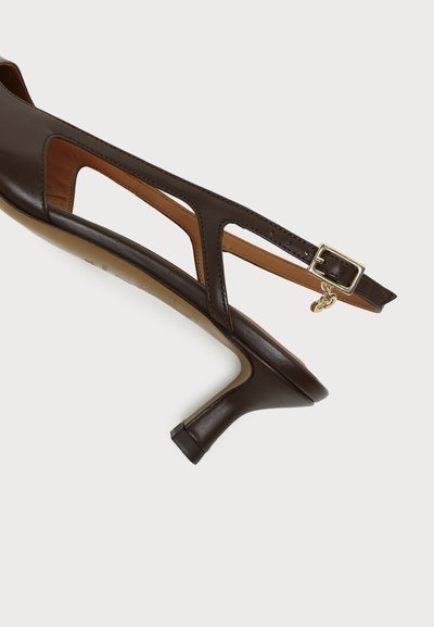 Mørkebrun lær slingback-hæl med utskårne sider, gullspenne og liten sjarm på stroppen, vist mot hvit bakgrunn.