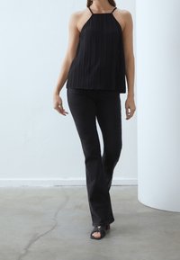 Haut à col halter plissé noir avec des bretelles fines, associé à des jeans noirs évasés et des sandales à talons. Textures lisses et design minimaliste.