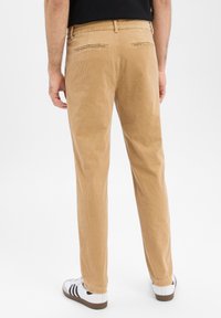 Spodnie sztruksowe w jasnobrązowym kolorze o prostym kroju, z dwoma tylnymi kieszeniami, zestawione z białymi trampkami. Materiał ma prążkowaną i miękką teksturę.