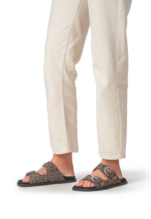 Bruine slippers met patroon en een gestructureerd materiaal, voorzien van dubbele banden en decoratieve gespen, gecombineerd met lichtgekleurde cropped broeken.