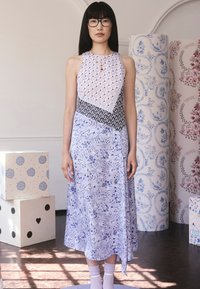 Virágmintás midi ruha világoskék és levendula színű anyagok keverékéből. Magas nyakkal és aszimmetrikus szegéllyel rendelkezik.