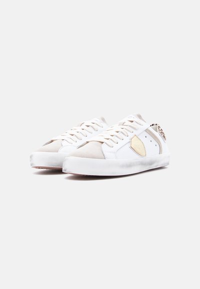 Baskets blanches avec des accents en daim beige, dotées d'une finition en cuir lisse, d'un détail texturé au talon et de lacets traditionnels. Semelle en caoutchouc grossier.