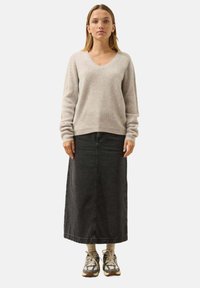 Maglione lavorato a costine grigio chiaro con scollo a V, abbinato a una gonna maxi in denim scuro. Il modello indossa calze beige e sneakers con fantasia.
