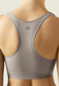 Grå sports-bh med racerback-design, glat tekstur og subtilt logo på ryggen. Syede sømme er synlige.