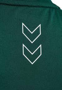 Camiseta deportiva verde con textura acanalada, que presenta un logo de doble chevrón blanco en la parte posterior. Sin otros detalles o patrones visibles.