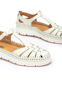 Sandalias de cuero blanco con correas trenzadas; plantilla acolchada; interior tostado; suela de goma con un leve tacón; detalles de costura a lo largo de los bordes.