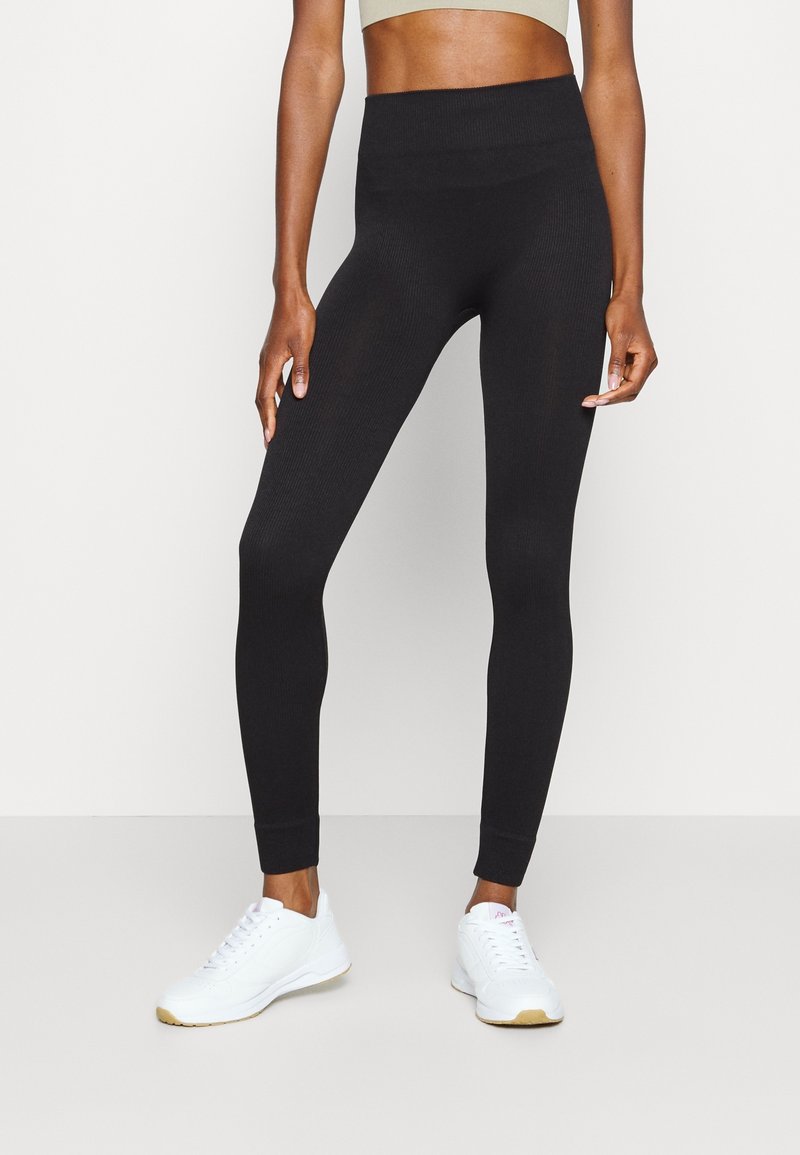 Svarta ribbade leggings med hög midja och muddar, tillverkade av elastiskt tyg, ihop med vita träningsskor.