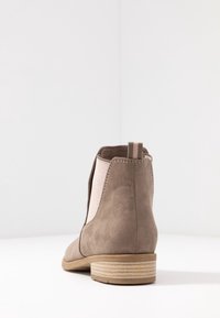 Brown suede ankle boot with elastic side panels, round toe, and a low stacked heel. Back pull tab for easy wearing.