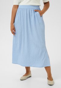 Light blue, textured maxi skirt with elastic waistband, side slit, and pockets. Paired with nude flats, featuring a rounded toe.