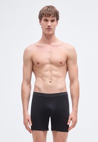 Juodi bokso šortai su minkštu, elastingu juosmeniu ir prigludusia forma, pagaminti iš lygaus, tamprios medžiagos, be matomų raštų.