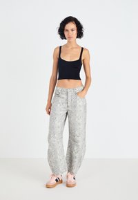 Zwarte cropped tanktop, loszittende slangenprintbroek in lichtgrijs, met zakken. Roze sneakers met zwarte strepen maken de outfit af.