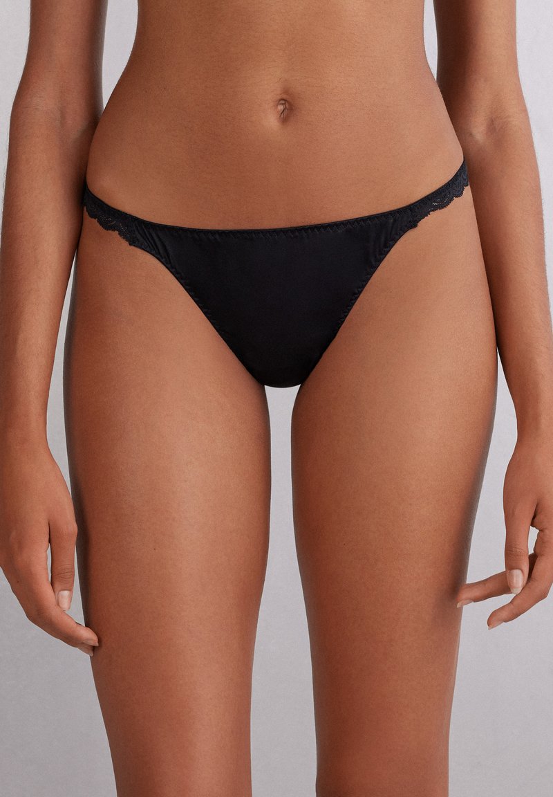 Zwarte stringonderbroek met kantafwerking, naadloze randen en zachte stof. Ontworpen voor minimale bedekking en een soepele silhouet.