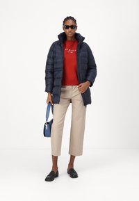 Navy puffer jacket, red sweatshirt, beige cropped trousers, black loafers, and blue handbag. Accessories include black sunglasses.
