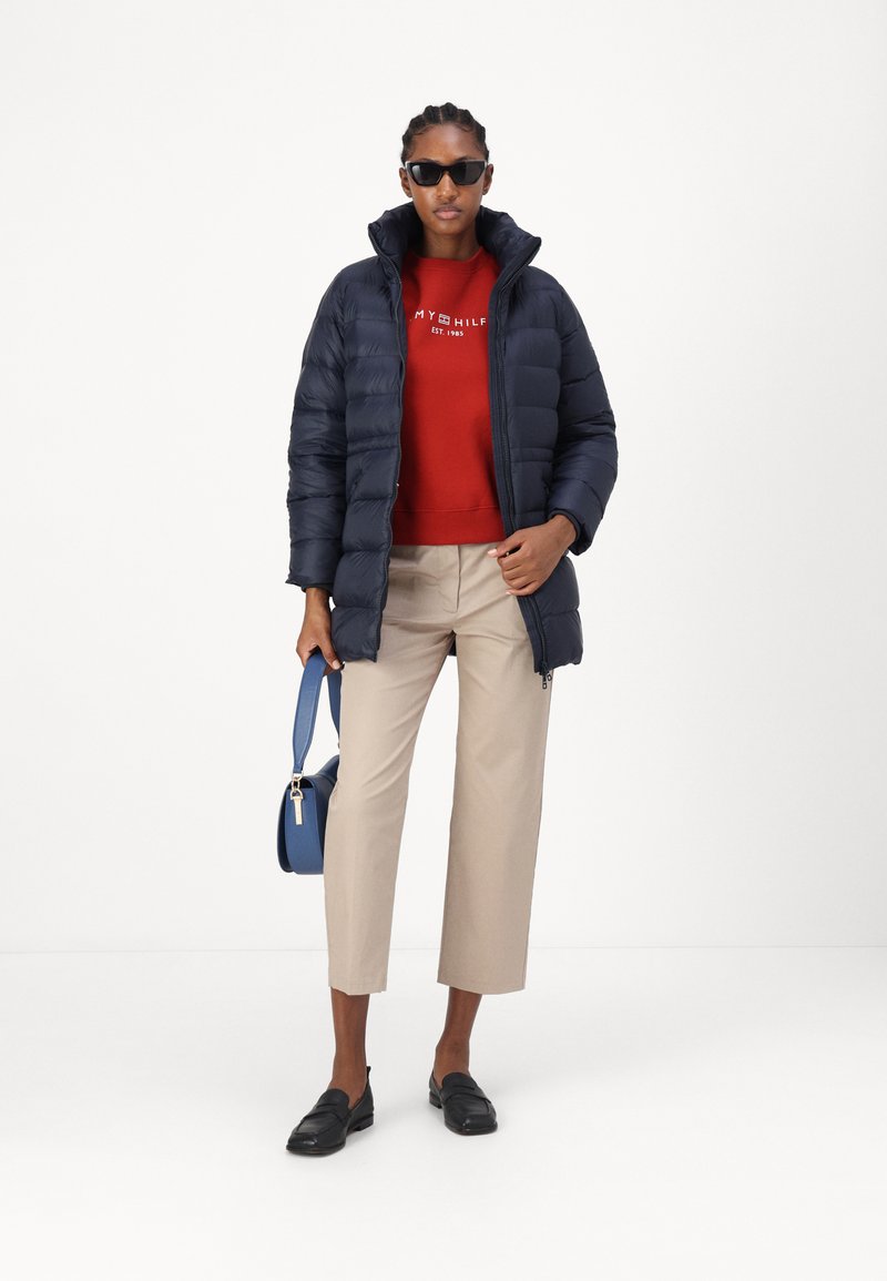 Marineblaue Pufferjacke, roter Sweatshirt, beigefarbene cropped Hose, schwarze Loafers und blaue Handtasche. Die Accessoires umfassen schwarze Sonnenbrille.