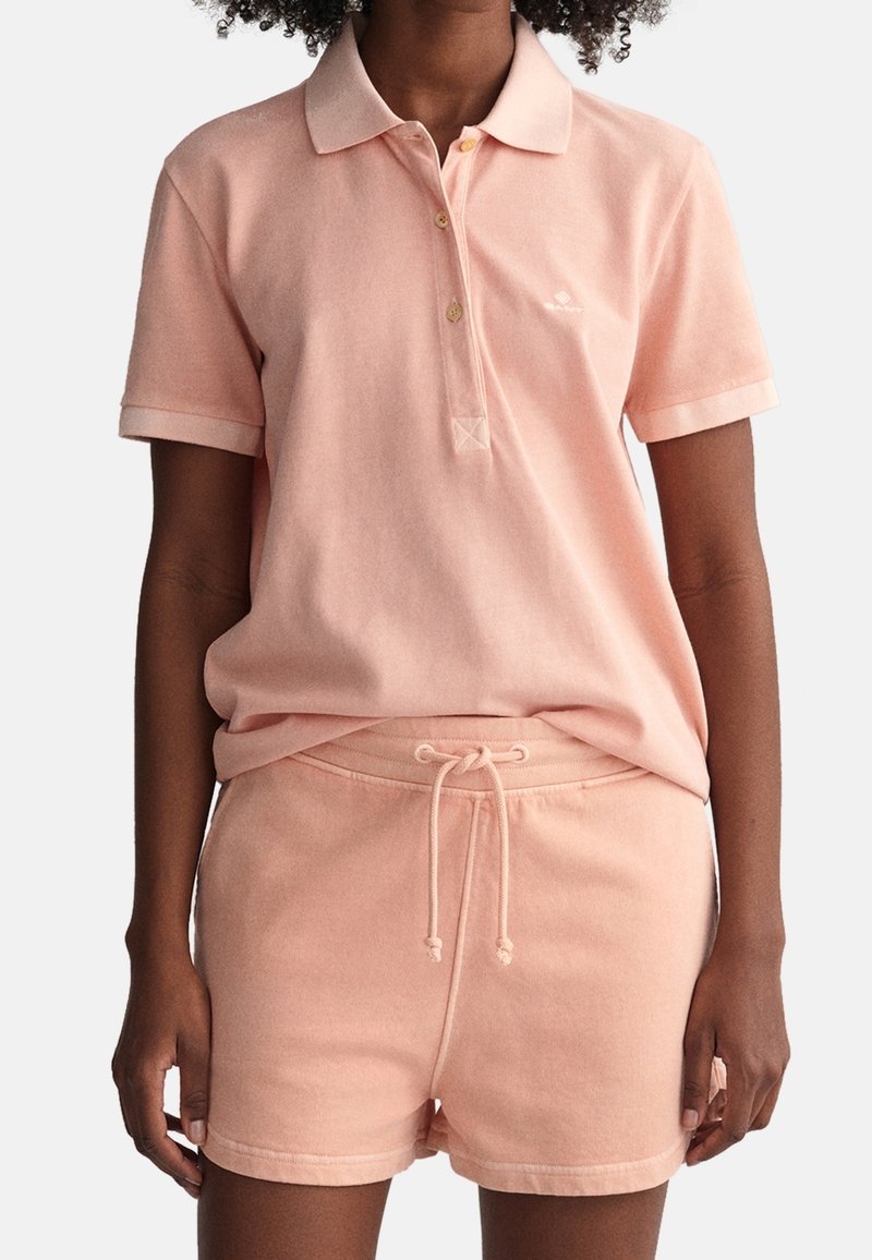 Personne portant un polo rose clair à manches courtes et un short assorti à cordon avec une coupe décontractée.