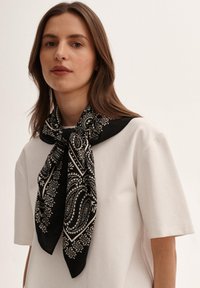 Czarna i biała chusta w wzór paisley o gładkiej fakturze, związana wokół szyi, w połączeniu z prostą białą koszulką.