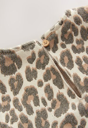 Bomuldstof med leopardprint i beige, brune og sorte farver. Har lukning med knapper og en lille slids ved halsudskæringen.