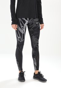 Leggings sportivi neri con un motivo geometrico grigio, realizzati in un materiale elastico. Abbinati a una maglietta nera a maniche lunghe e sneakers nere.