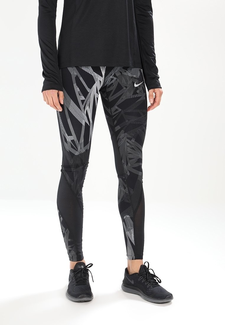 Leggings sportivi neri con un motivo geometrico grigio, realizzati in un materiale elastico. Abbinati a una maglietta nera a maniche lunghe e sneakers nere.