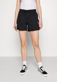 Černé kraťasy s elastickým pasem a šňůrkou, vybavené dvěma bočními kapsami. V kombinaci s černobílými kostkovanými teniskami.