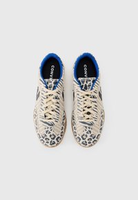 Baskets beiges avec tissu rayé et accents imprimé léopard, dotées d'une doublure bleue et d'un logo noir. Lacets plats et semelle en caoutchouc texturée.
