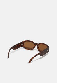 Tortoiseshell sunglasses with brown lenses, angular frames, and thick temples featuring a subtle logo accent on the side.