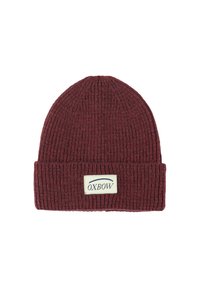 Bonnet en tricot bordeaux avec une texture côtelée, présentant un revers et une étiquette rectangulaire avec "OXBOW" en bleu sur un fond crème.