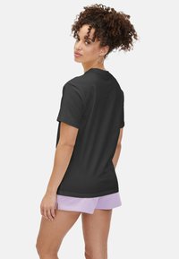 Camiseta de algodón negra con mangas cortas y escote redondo, combinada con pantalones cortos de color morado claro. La modelo tiene el cabello rizado y lleva puesto un mínimo de joyas.